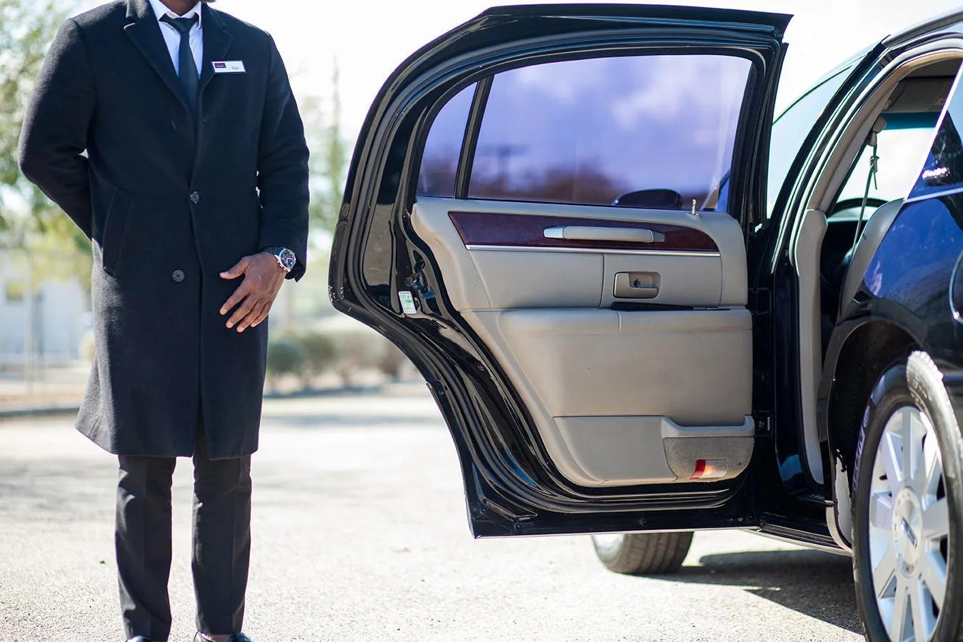 Professional chauffeur in dark suit standing beside black luxury sedan