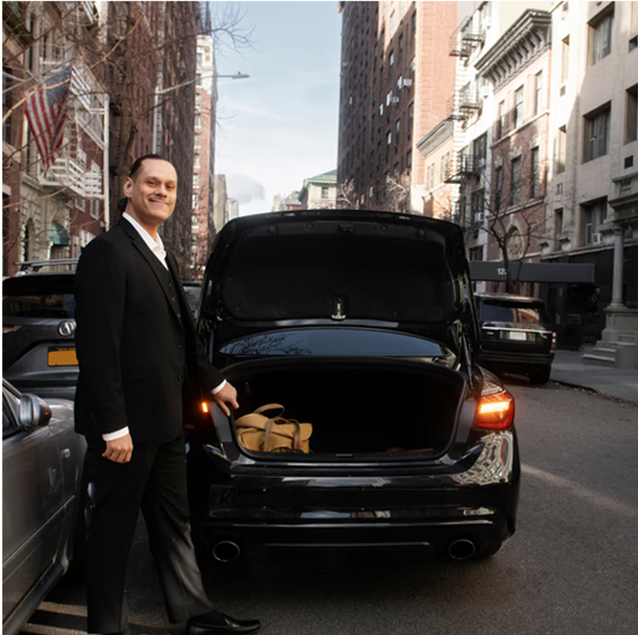 Male chauffeur in professional attire standing next to luxury car on city street